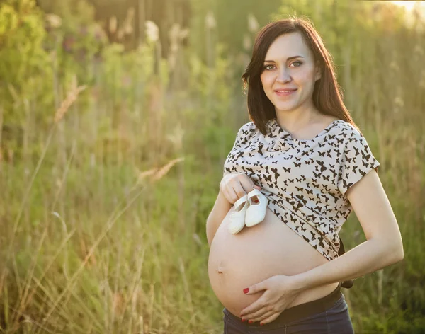 Gravid kvinna med baby skor lite på sin mage — Stockfoto