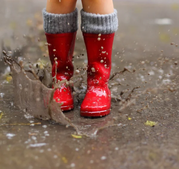 赤い雨を着て子供ブーツ水たまりにジャンプ — ストック写真