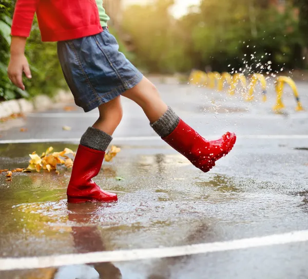 Dziecko nosi czerwony deszcz buty, skoki w kałuży — Zdjęcie stockowe