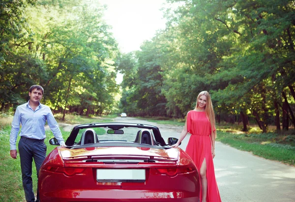 Junges glückliches Paar steht neben rotem Auto — Stockfoto