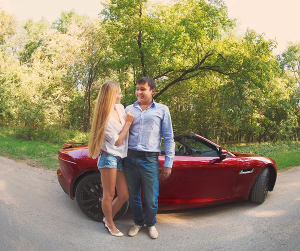 Young happy couple standing near red car — Stock Photo, Image