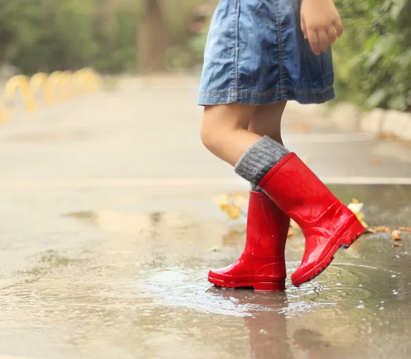 Criança usando botas de chuva vermelha pulando em uma poça — Fotografia de Stock