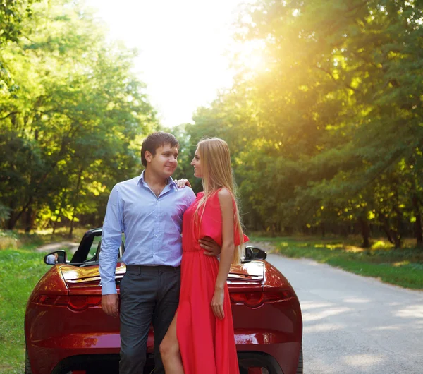 Jonge gelukkige paar in de buurt van de rode auto — Stockfoto