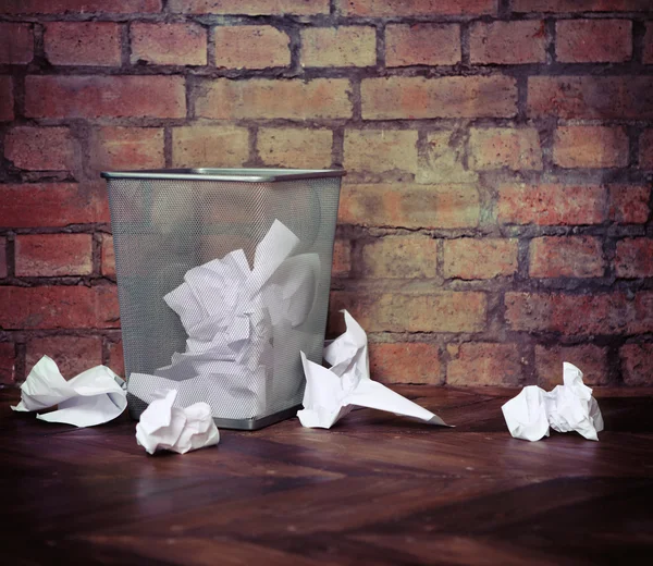 Papelera de reciclaje llena de papeles arrugados. Fondo de pared de ladrillo — Foto de Stock