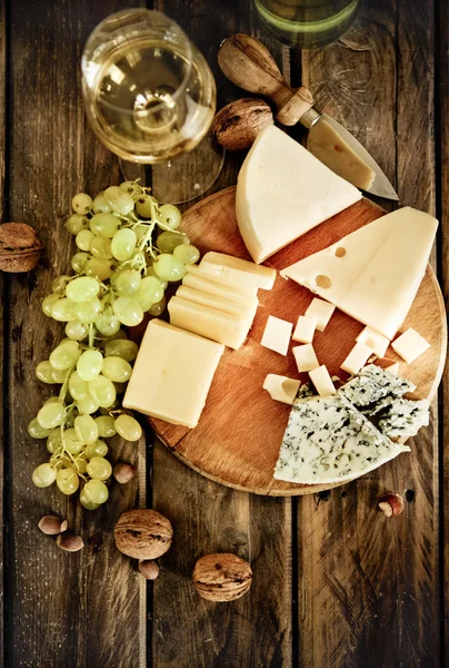 Bottles and glass of white wine, cheese, nuts and grapes — Stock Photo, Image