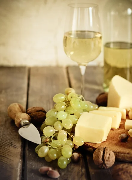 Botellas y copa de vino blanco, queso, frutos secos y uvas — Foto de Stock