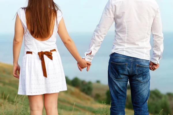 Pareja joven enamorada cogida de la mano. Fondo marino de verano — Foto de Stock