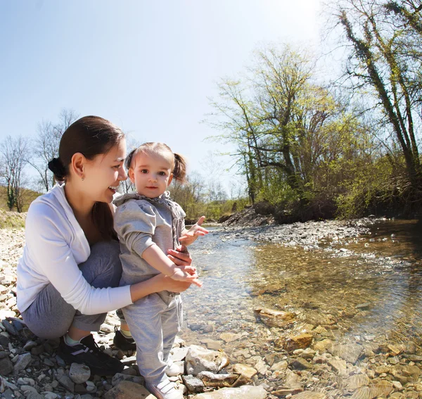 Felice giovane madre con figlioletta vicino al fiume di montagna — Foto Stock