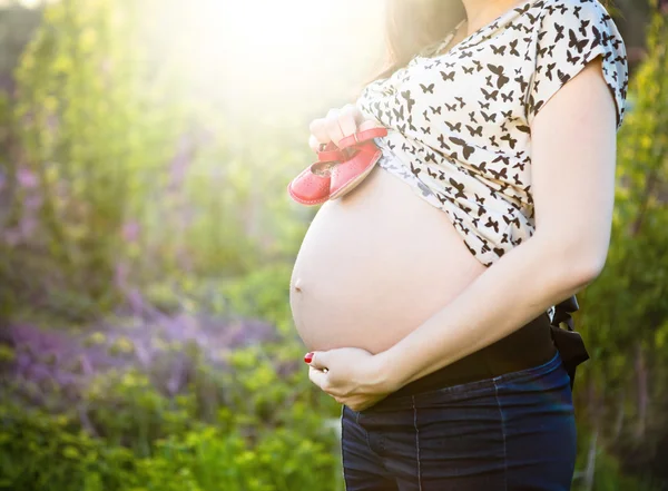 Primer plano de una mujer embarazada irreconocible con zapatos pequeños para bebés — Foto de Stock