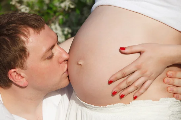 Unga lyckliga gravida par i den blommande vår parken — Stockfoto