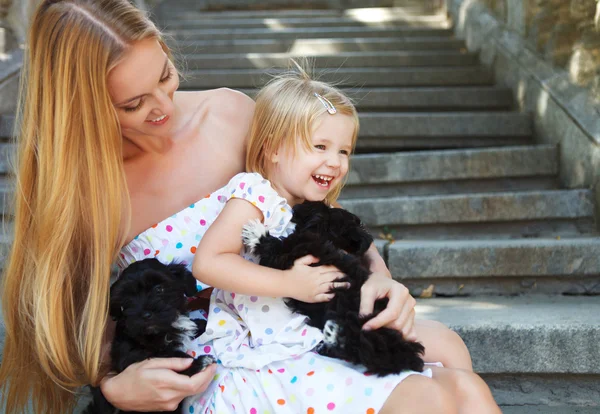 Мила дівчинка і її мати обіймають цуценят собак — стокове фото