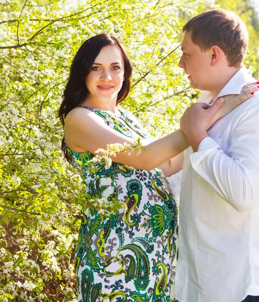 Jovem casal grávida feliz no parque de primavera florido — Fotografia de Stock