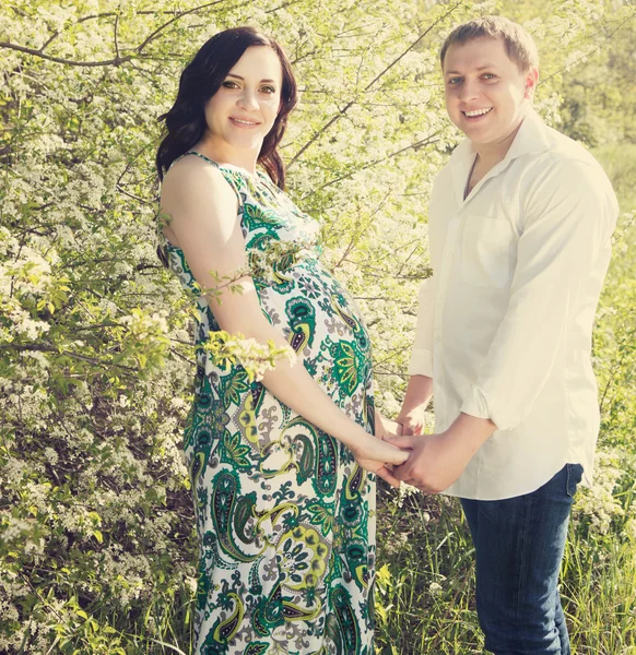 Young happy pregnant couple in the flowering spring park — Stock Photo, Image