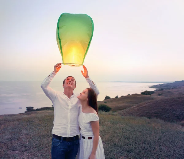 Casal jovem iniciar uma lanterna verde céu chinês no crepúsculo — Fotografia de Stock