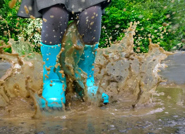 Criança usando botas de chuva azul pulando em uma poça — Fotografia de Stock