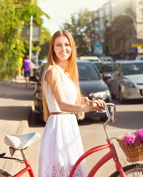 Söt blond tjej med retro-look, cykel och korg med blommor — Stockfoto