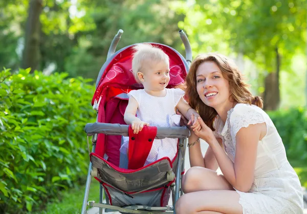 Beautiful young woman with her child in a baby carriage — Stock Photo, Image