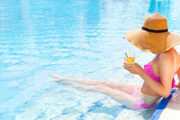 Mujer bonita en un sombrero disfrutando de un cóctel en una piscina — Foto de Stock