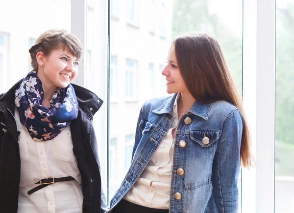 Två lyckliga kvinnliga studenter pratar nära fönstret — Stockfoto