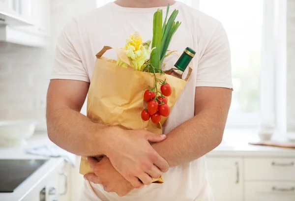 Uomo in possesso di sacchetto di carta pieno di generi alimentari in cucina — Foto Stock