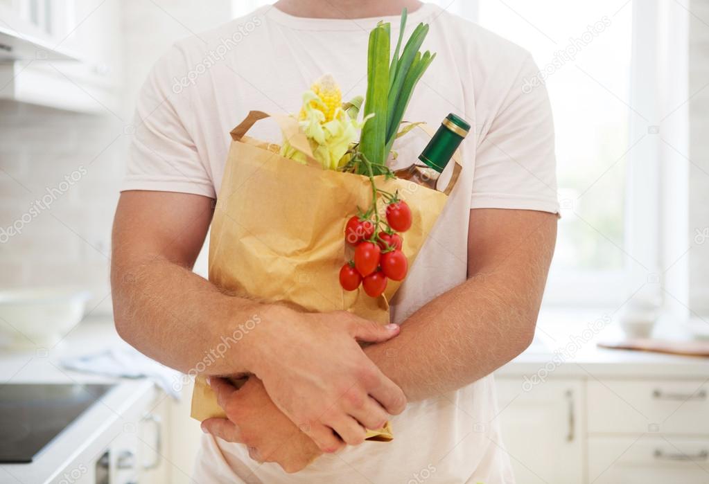 Man holding paper bag full of groceries on the kitchen 