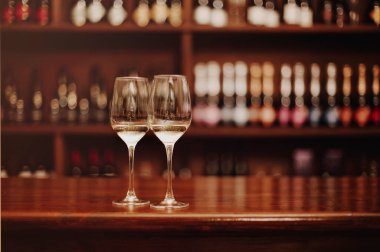 Ahşap bar masasında iki bardak beyaz şarap. Sıcak renklerde fotoğraflar. Bir kadeh şaraba odaklan. Sevgililer Günü, randevu, aşk, kutlama