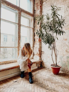 Sepia tarzı karamsar bir fotoğraf. Uzun elbiseli, eski püskü bir odada elinde eski bir kamera olan, terk edilmiş bir evde terk edilmiş tuğla duvara karşı saksı yeşili bir bitki taşıyan bir kadın.