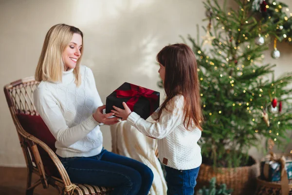 可爱的女儿送给她年轻微笑的妈妈圣诞礼物 她和装饰过的树一起坐在房间里 快乐的家庭妈妈和孩子们穿着白色针织毛衣在家里庆祝新年 — 图库照片
