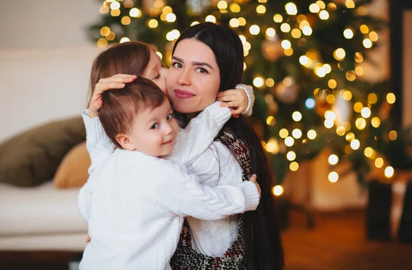 在圣诞节庆祝活动期间 年轻妇女带着孩子在针叶树旁拥抱 — 图库照片