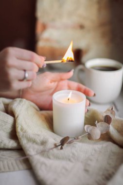 Evde rahatlık ve rahatlık için pencere eşiğinde yanan mum yakan bir kadın eli, soğuk mevsimde sıcak ve samimi bir atmosfer yaratmaya çalışan bir kadın. Hygge yaşam tarzı konsepti
