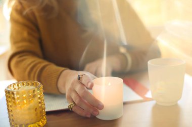 Masada elinde yanan bir mumla oturan bir kadının bulanık görüntüsü iş yerinde rahat bir ortam yaratıyor. Farkındalık meditasyonunu aromaterapi ile pratik yapmak