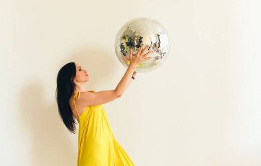 Uzun saç stili ve parlak makyajlı esmer bir kadının portresi. Ellerinde büyük, parlak bir disko topu var. Etrafındaki her şeyi yansıtıyor.