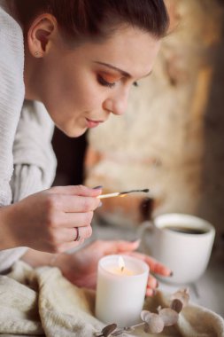 Evde rahatlık ve rahatlık için pencere eşiğinde yanan mum yakan bir kadın eli, soğuk mevsimde sıcak ve samimi bir atmosfer yaratmaya çalışan bir kadın. Hygge yaşam tarzı konsepti