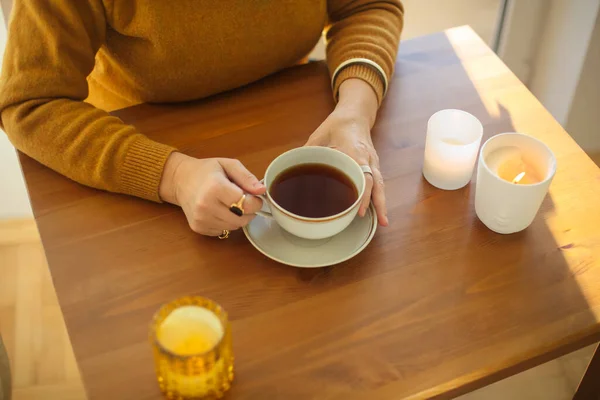 Elinde Çay Fincanı Olan Bir Kadının Yanan Mumlarla Masada Oturduğu — Stok fotoğraf