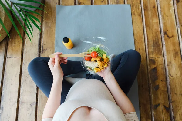 怀孕期间的健康生活方式和营养 美丽的孕妇坐在瑜伽垫上 泰然自若地吃着沙拉 微笑的女性期待着婴儿在家里吃着健康的午餐 顶部视图 — 图库照片