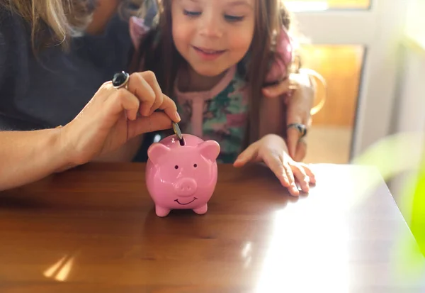 Little Girl Putting Coin Piggy Bank While Sitting Table Mother — Stock Photo, Image