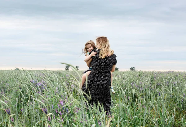 緑の牧草地で抱擁フィールドの花花束を持つ幸せな母親と娘 母親は野外で小さな娘を抱きかかえている 愛と家族の概念 — ストック写真