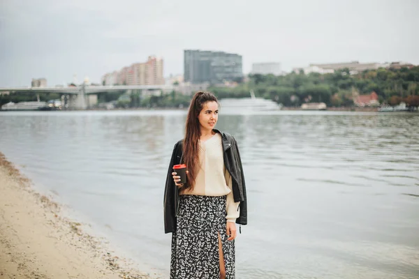 秋天的一天 穿着休闲装 背着咖啡 背景是城市景观的年轻女子 在海滨欣赏大自然的浪漫梦幻女子 — 图库照片