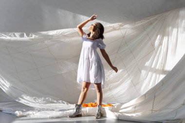 Atla ve uç. Gri stüdyo arka planında izole edilmiş büyük beyaz kumaşla havaya atlayan kaygısız Afrikalı Amerikalı genç bir kadın. Yaşam kavramı için özgürlük ve susuzluk