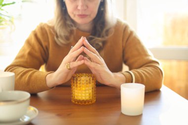 Masada elinde yanan bir mumla oturan bir kadının bulanık görüntüsü iş yerinde rahat bir ortam yaratıyor. Farkındalık meditasyonunu aromaterapi ile pratik yapmak