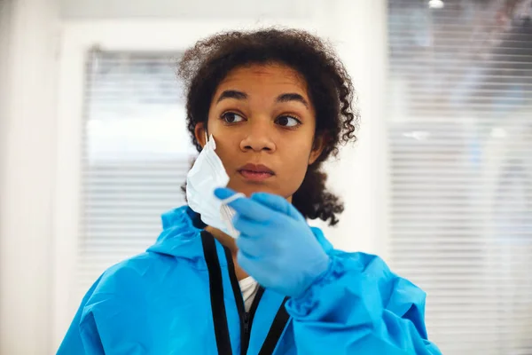 身穿防护服的年轻疲惫的非洲裔美国医务工作者或护士的画像 摘下面具 带着沮丧的表情望向远方 Covid 19大流行病期间的保健工作者 图库图片