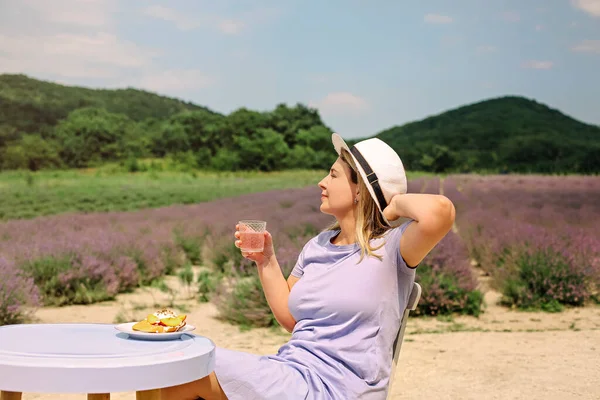 麦藁帽子の女性は ラベンダー畑のテーブルに座ってレモネードを飲み 桃とチーズでブルスケッタを食べる 夏休み 休日のコンセプト — ストック写真