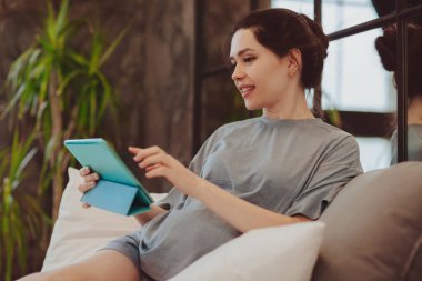 Genç, gülümseyen hamile bir kadın dijital bir masa tutuyor ve evde otururken video görüşmesi yapıyor. Ailesi ya da arkadaşlarıyla internette konuşuyor. Uzaktan doğum öncesi kontrol ve danışma kavramı