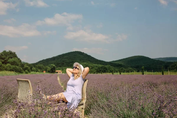 모자를 금발의 여자가 라벤더밭 가운데앉아 의자에서 긴장을 아름다운 아름다운 언덕을 스톡 사진