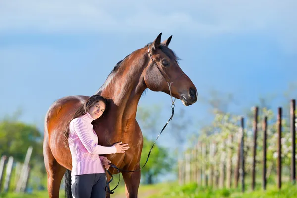 Jovem menina bonita de pé com um cavalo no jardim — Fotografia de Stock