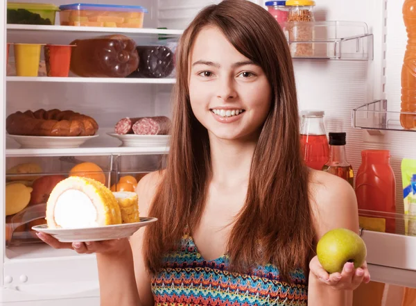 Молодая женщина с яблоком и тортом на заднем плане холодильника — стоковое фото