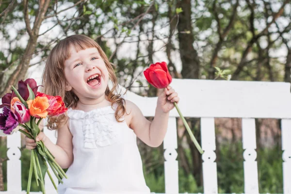 Menina feliz com tulipas no banco de madeira branco — Fotografia de Stock