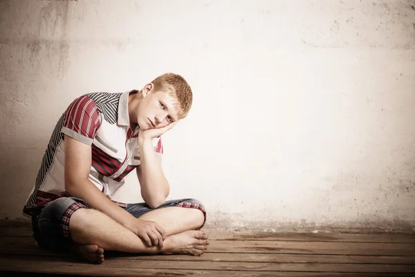 Sério adolescente menino sentado no velho chão de madeira — Fotografia de Stock