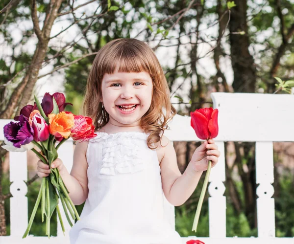 Happy girl with tulips on white wooden bench — Stock Photo, Image