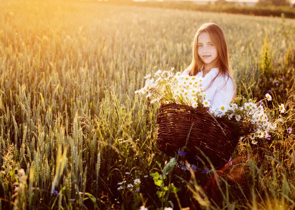 Girl in the wheat field with basket of flowers — Stock Photo, Image